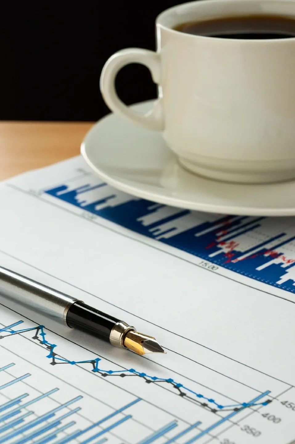 Close-up of a business report with a declining line graph, a pen, and a white coffee cup and saucer